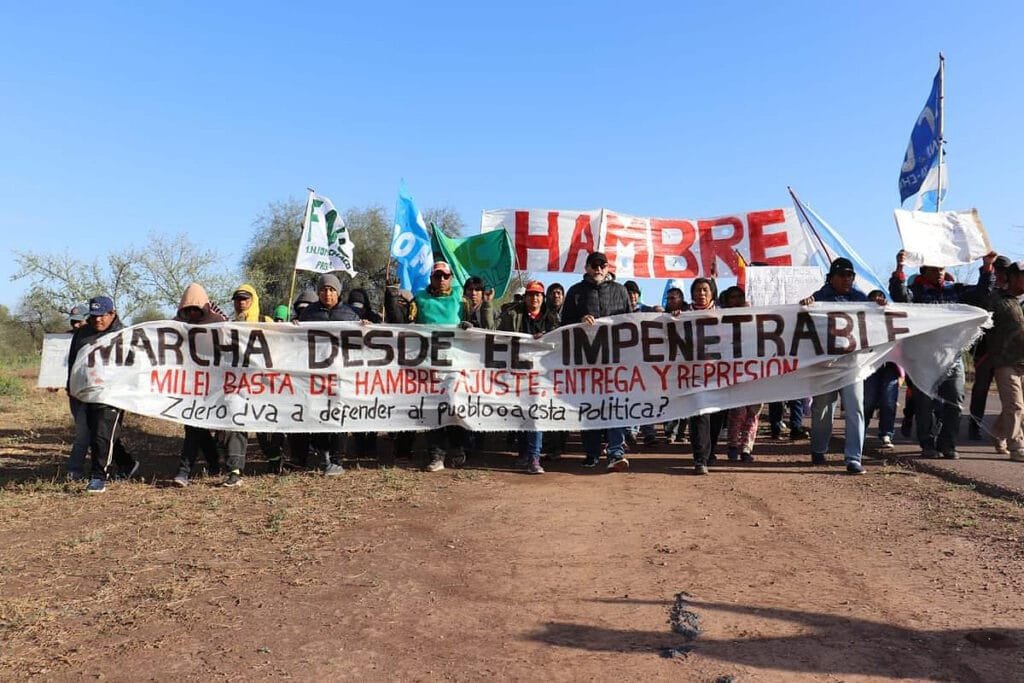 En la imagen se ve a un grupo de manifestantes pertenecientes a la Multisectorial de El Impenetrable durante una marcha realizada el 13 de agosto de 2024 en la provincia de Chaco, Argentina. La manifestación, organizada en una zona vulnerable del país, surge como respuesta a la pobreza extrema, el hambre y la crisis económica que enfrenta la población local. En la pancarta principal, se puede leer el reclamo dirigido contra el gobierno de Javier Milei: "Milei, basta de hambre, ajuste, entrega y represión". El cartel también cuestiona la postura del gobernador Jorge Capitanich con la pregunta: "¿Zero va a defender al pueblo o a esta política?". Esta movilización forma parte de una serie de acciones destinadas a visibilizar la situación crítica que atraviesan las comunidades más desprotegidas del norte argentino .